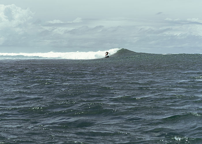 Surfer riding a wave across the vast sea under a cloudy sky, capturing the spirit of adventure and caution at sea.