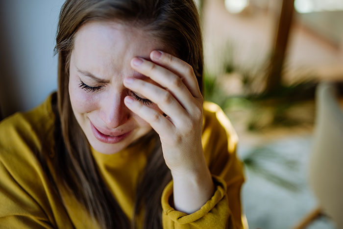 Young woman in a yellow sweater appears upset, resting her head on her hand.