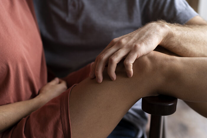 Two people in casual outfits with a hand resting on a knee, capturing an intimate moment during a long flight.