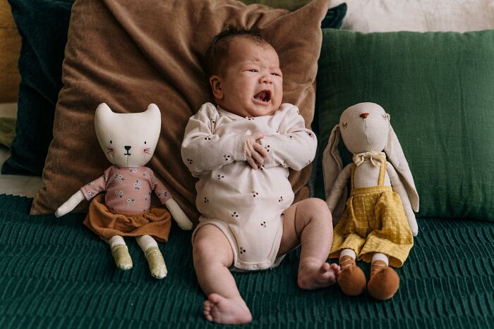 Crying baby on a couch between two toys, emphasizing a worst experience similar to a long flight discomfort.