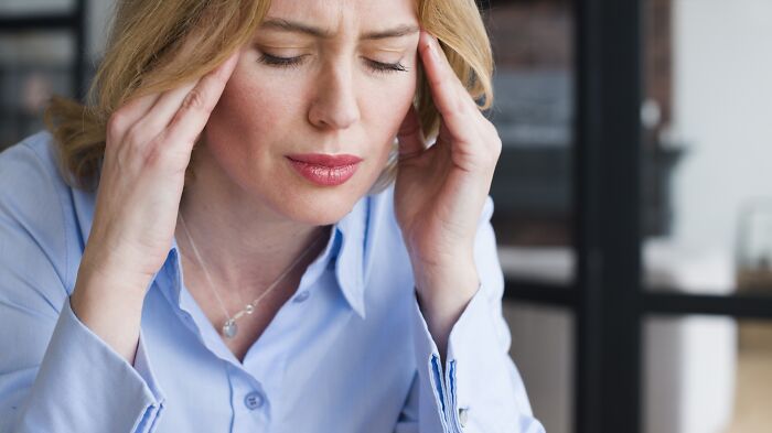 Woman in blue shirt experiencing discomfort, holding her head, illustrating the worst experience on a long flight.