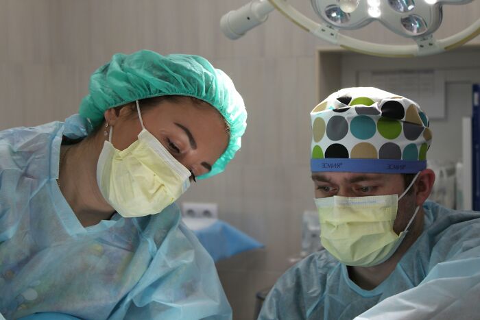 Two surgeons in a well-lit operating room, wearing masks and scrubs, focusing intently on a medical procedure.