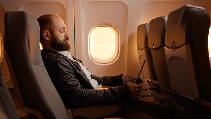 Man experiencing discomfort in an airplane seat during a long flight.