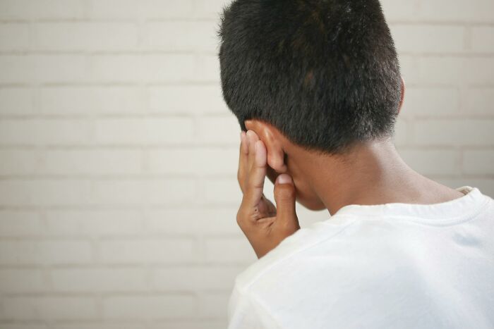 Person in discomfort on a flight, holding their ear against a brick wall background.