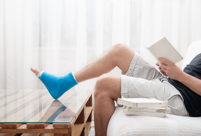 Man with blue foot cast reading on a couch, reflecting a worst experience from a long flight.