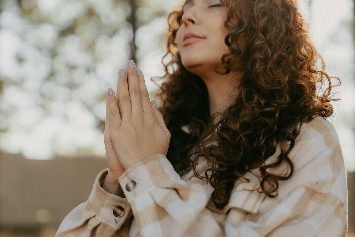 Person in a plaid shirt with eyes closed, hands in prayer, reflecting on worst experience during a long flight.