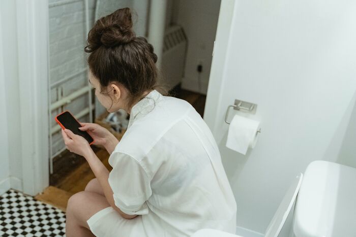 Person sitting on a toilet using a smartphone, capturing a worst-experience during a long flight.