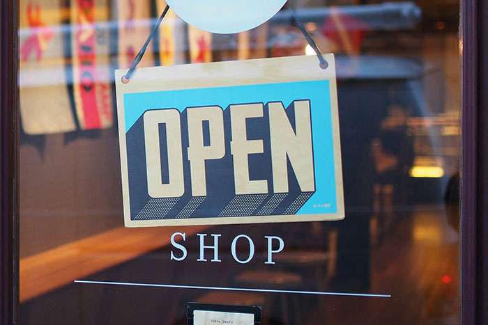 "Open sign hanging on shop door, reflecting a bustling street scene, perfect for a Secret Santa gift exchange."