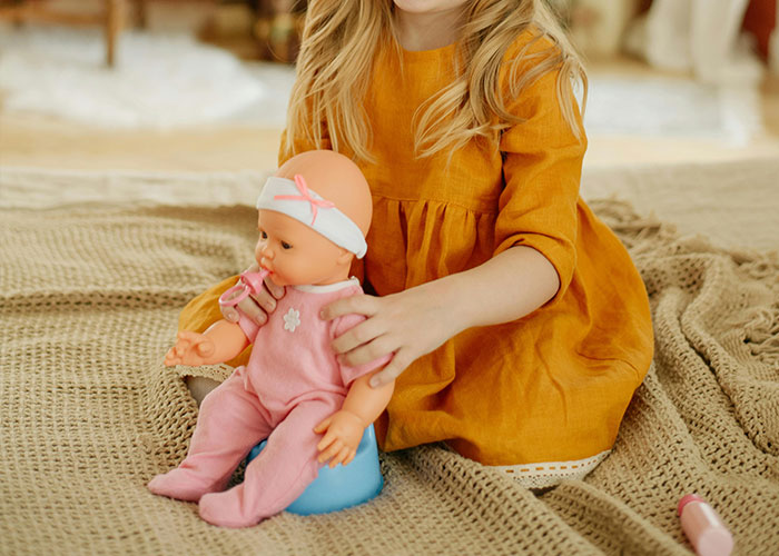 Child in an orange dress playing with a doll on a textured blanket during Christmas.