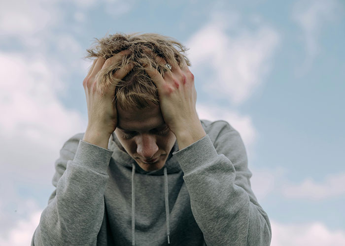 Man in gray hoodie outdoors holding head, stressed about worst Christmas events.