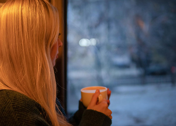 Woman looking out window with a mug, reflecting on worst things during Christmas.