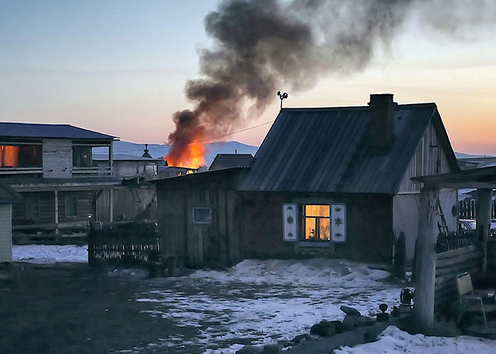 House on fire during Christmas evening, with dark smoke rising, surrounded by snow-covered ground, depicting a worst-case scenario.