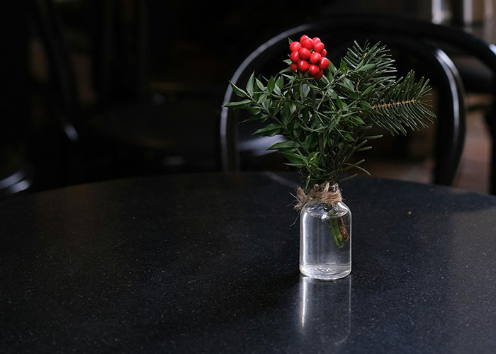 A small vase with Christmas greenery and red berries on a black table, symbolizing holiday misfortune.