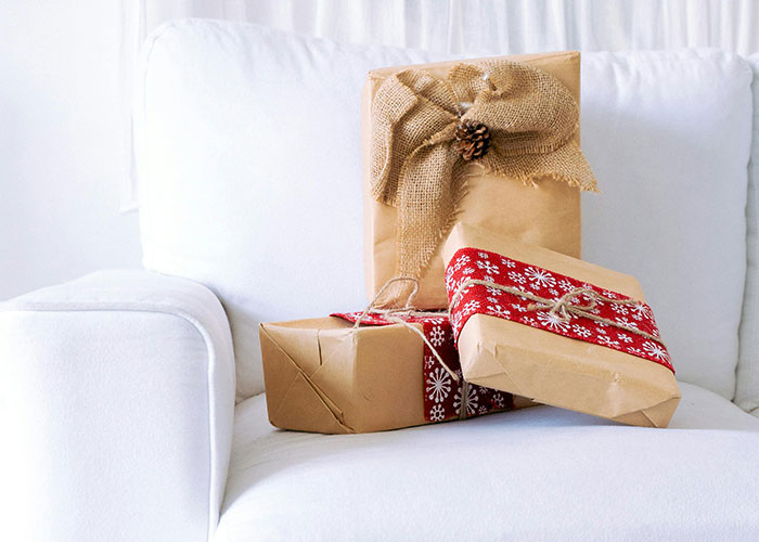 Wrapped Christmas gifts on a white couch with a rustic burlap bow and festive red ribbon.