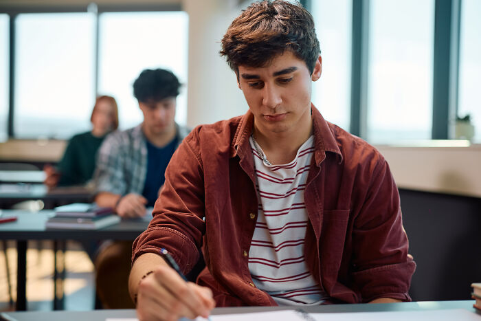 Astonished student in class taking notes, wearing a red shirt, focused on the task.