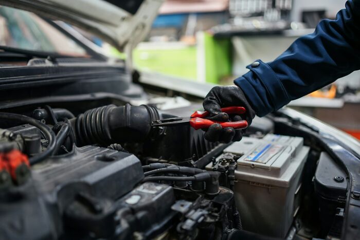 Mechanic working on a car engine with red pliers, showcasing repair skills in an automotive setting.