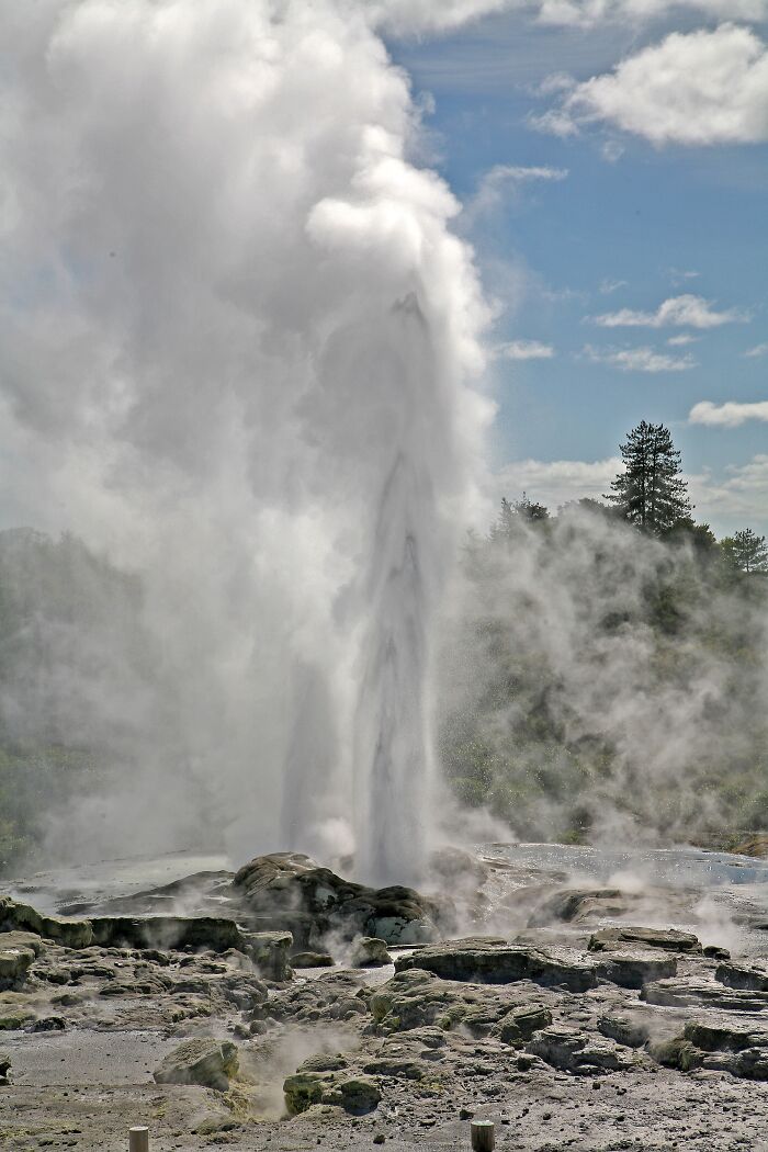 Geyser erupting against a blue sky, showcasing stunning natural phenomena.