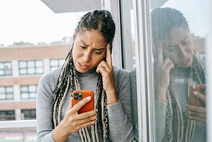 Pet sitter looks at phone, appearing frustrated, with a city background reflecting in the glass window.