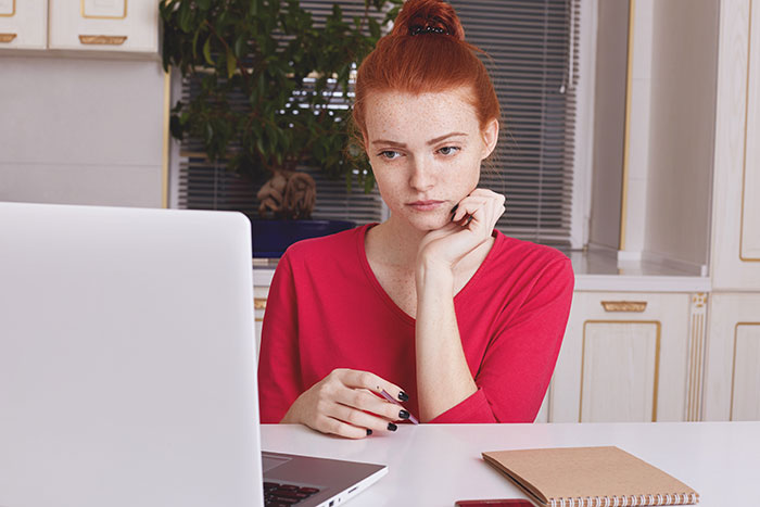 Woman in red shirt looking at laptop, reflecting on email style being perceived as rude and unprofessional.