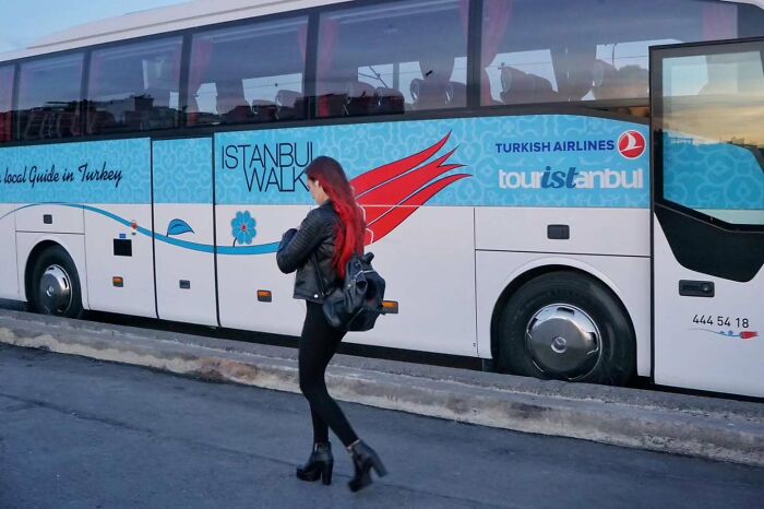 Street photographer captures a woman with red hair walking past a bus with wings design.