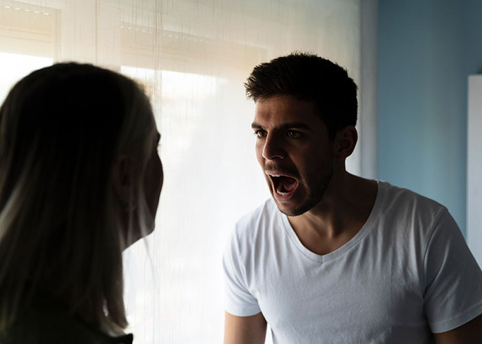 Man angrily shouting at a woman in a tense confrontation near a window.