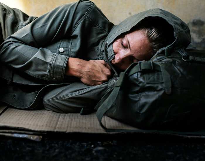 Person sleeping on a cardboard sheet in a jacket, highlighting officer-corruption impacts.