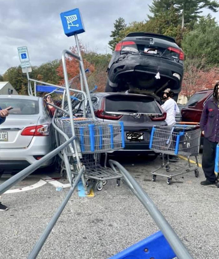 Two cars in a parking lot accident, with one vehicle on top of the other near shopping carts, showcasing classic Idiots-In-Cars scenario.