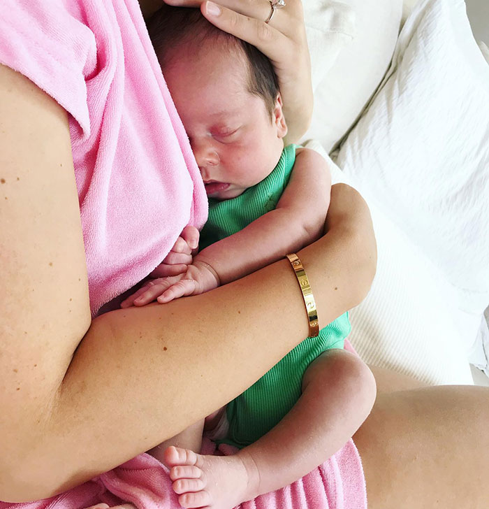 A person in a pink robe lovingly cradling a sleeping baby wearing green.