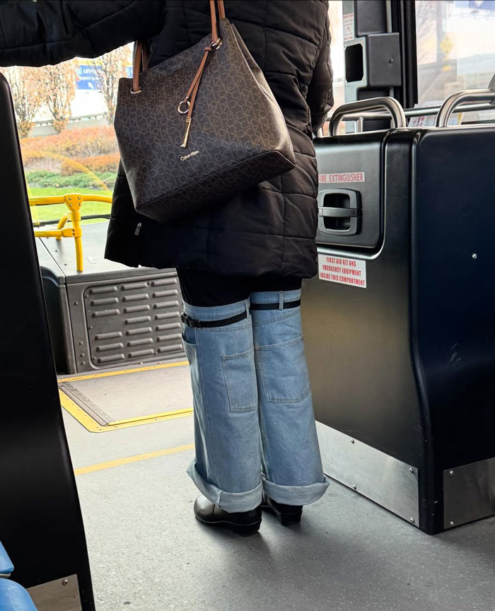 NYC local on a bus wearing layered wide-leg jeans and black jacket, with a designer handbag, showcasing bold fashion.