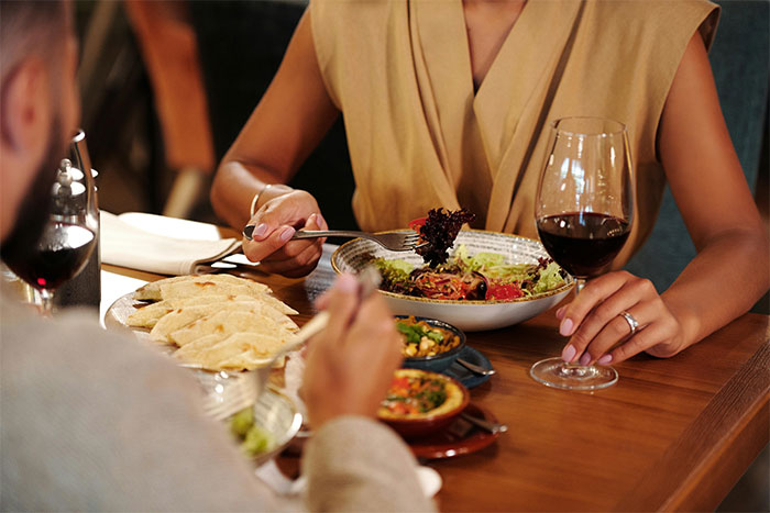 Couple dining at a restaurant table, sharing a meal with wine, focusing on salad and tortilla dishes.