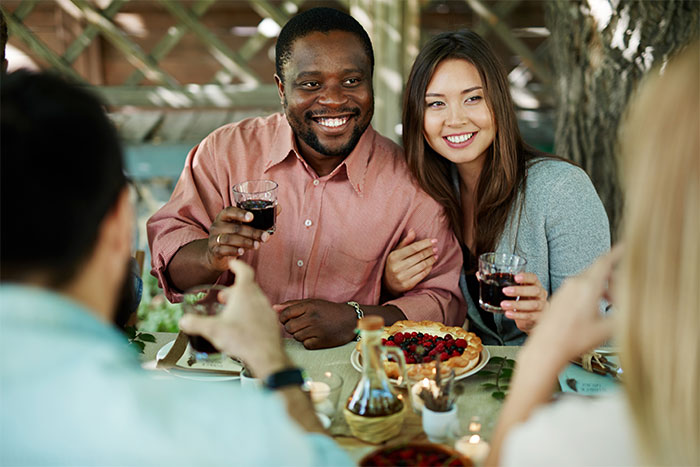 Friends at an outdoor gathering, smiling and holding drinks, casually dressed amidst a relaxed setting.