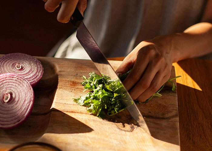 Person chopping vegetables on a wooden board, highlighting a vegetarian meal preparation.