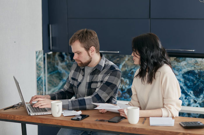 Two people at a table, one on a laptop, discussing a topic related to revenge, with coffee cups and papers.