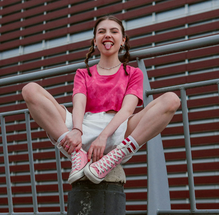 Person sitting playfully on a railing, wearing a pink shirt and sneakers, embodying life hacks and youthful energy.