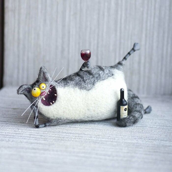 Strange art doll of a funny-looking animal, resembling a cat, holding a wine glass, created by a Georgian artist.