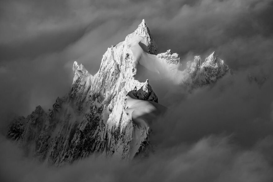 Award-winning wildlife photo of a dramatic, snow-covered mountain peak surrounded by clouds.