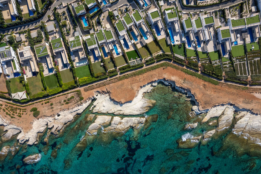 Aerial view of coastal village with modern houses and rocky shoreline, showcasing European Photographer of the Year contest.