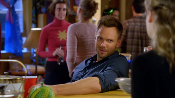 Man in blue shirt at a lively party, talking with a woman, representing beloved shows enjoyed repeatedly.