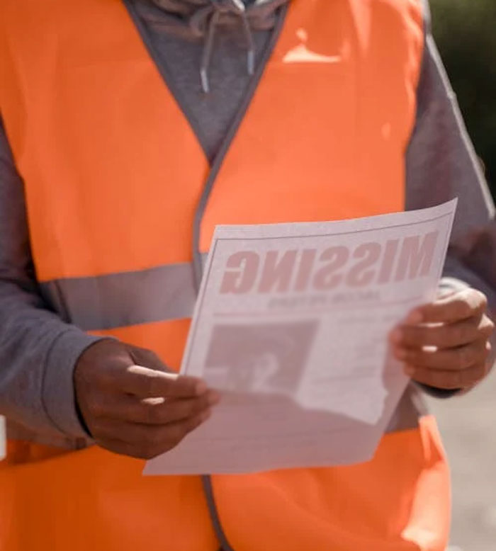 Person in orange vest holding a "Missing" poster, related to unsolved true crime cold cases.