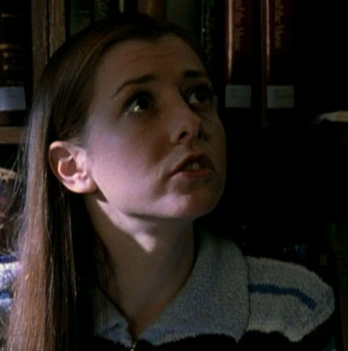 Young woman in a dimly lit room, looking upwards, wearing a striped sweater, illustrating talent in a pigeonholed role.