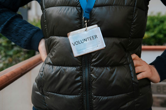 Person wearing a volunteer badge stands with hands on hips, showcasing a life hack for real-life engagement.