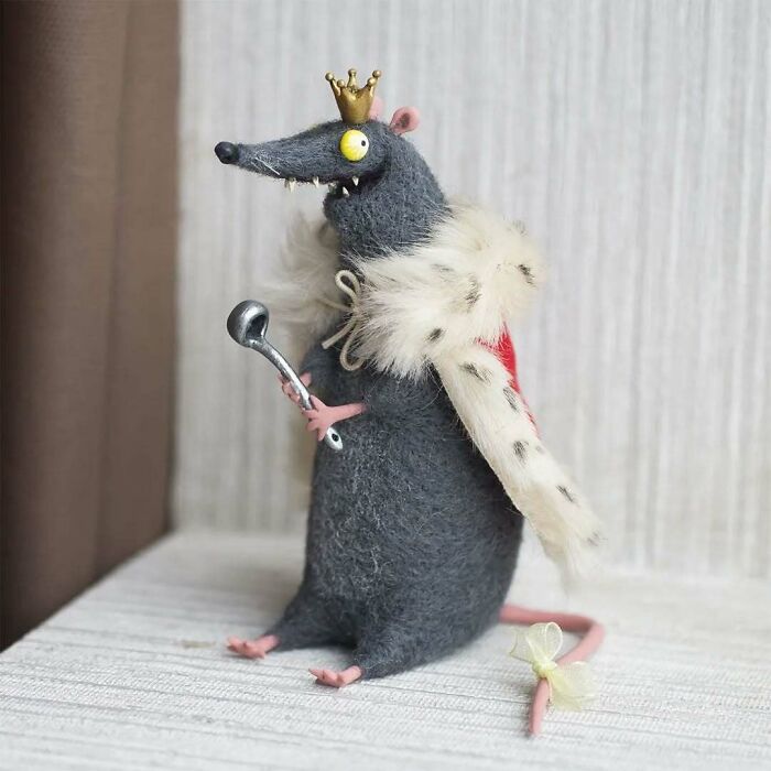 Funny-looking art doll of a rat wearing a crown and royal cape, holding a spoon, created by Georgian artist.