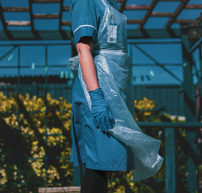 Person in protective gear, relevant to true crime cold cases, stands outdoors wearing blue gloves and apron.