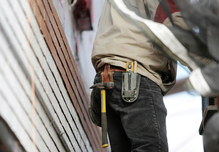 Person using quality hacks for construction with tools in a belt, working on siding.