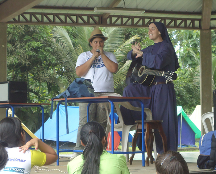 Nun with a guitar engaging with a crowd during an outdoor event under a pavilion.