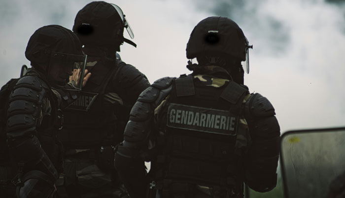 Gendarmerie officers in tactical gear, standing together amidst smoke.