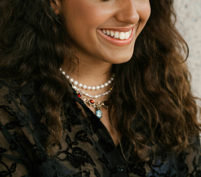 Smiling woman with curly hair, wearing pearl necklace, symbolizing untold family stories.