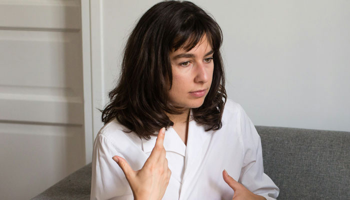 Person in a white shirt on a gray sofa, gesticulating passionately about true crime cold cases.