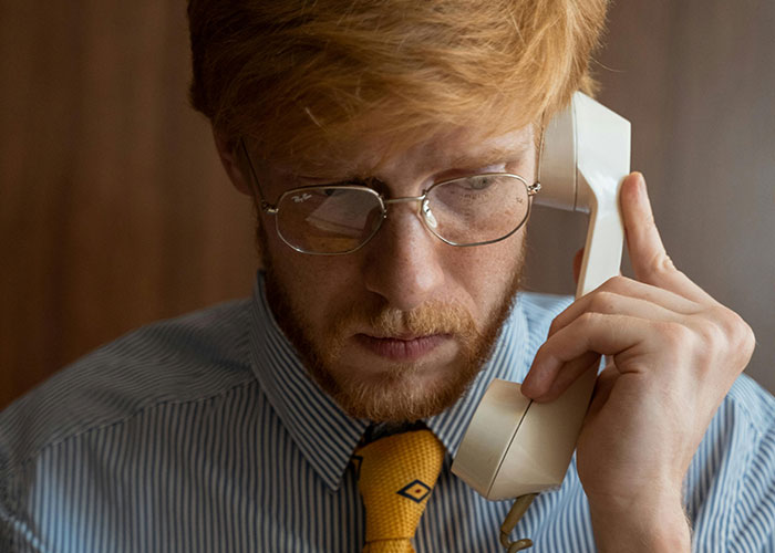 Man in glasses and striped shirt on phone, appearing tense; signifies awkward job interview moment.