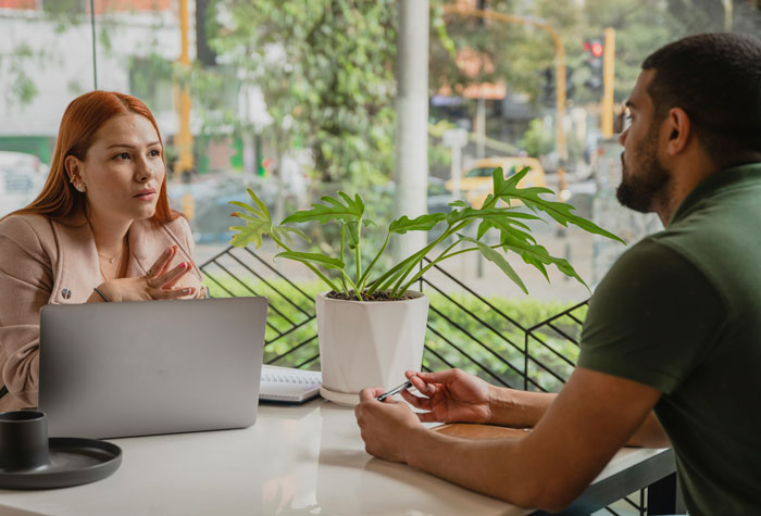 Two people discussing life hacks in a modern office setting with a laptop and a plant on the table.